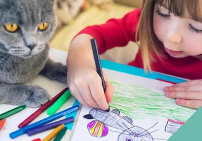 A grey cat lying by a little girl drawing