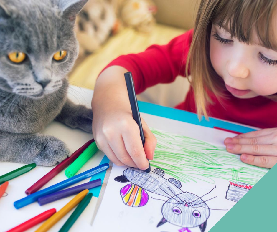 A grey cat lying by a little girl drawing